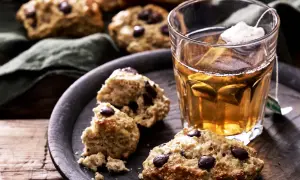 Nyttigare scones med chokladbitar på en mörk bricka bredvid ett glas te. Perfekt fika!