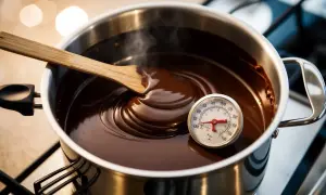 Smält choklad i kastrull med termometer. En träsked rör om den blanka, flytande chokladen. Perfekt för att temperera choklad.