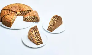 A sliced zebra cake with a marbled chocolate and vanilla pattern, served on white plates.