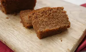 En bit mjuk pepparkaka med pudersocker på en träskärbräda.