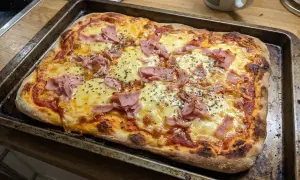 En nybakad pizza med skinka och ost på en plåt. Perfekt för en snabb middag med snabb pizzadeg!