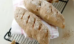 Två nybakade bröd, perfekta för ett skrädmjöl recept. Ligger på ett rutigt tyg på ett galler.