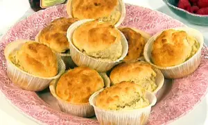 En rosa bricka med nybakade dinkelscones i pappersformar. Bredvid syns hallon och en burk sylt.