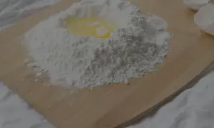 En hög mjöl med ett ägg i mitten, redo att blandas. Kanske lite för mycket bakpulver i receptet? Äggskal ligger bredvid.