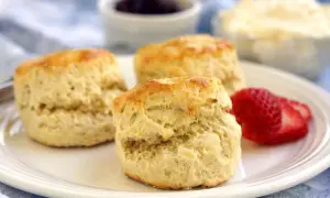 Tre fluffiga scones, ett perfekt scones grundrecept, serveras med jordgubbar och grädde.