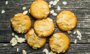 Små, gyllene mandelkakor, perfekta för ett bondkakor recept. Spridda mandelflagor på en rustik träyta.