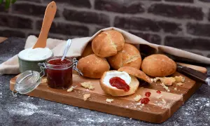 Färska scones havregryn med sylt och grädde på en träskärbräda.