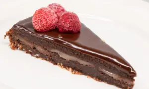 En bit kladdkaka med After Eight-smak, toppad med tre hallon på en vit tallrik.