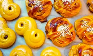 En närbild av saftiga lussebullar, vissa med russin och pärlsocker, andra med enbart russin. De ser otroligt goda ut!