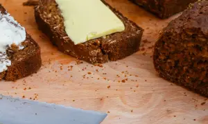 Mörkt bröd med smör och en skiva med yoghurt på en skärbräda.