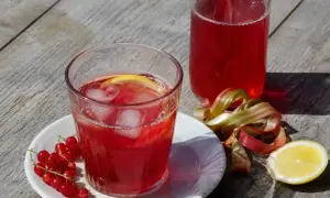 Ett glas med röd saft, is och citron, bredvid en flaska saft, röda vinbär och rabarber. Perfekt för att koka saft.
