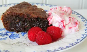 En bit kladdkaka med lakrits, serverad med hallon och grädde.