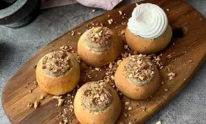Färdiga semlor med mandelmassa till, toppade med hackade nötter och en generös klick grädde på en av dem.