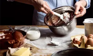 Händer blandar chokladsmet i skål. Ingredienser som smör, ägg och mjölkfri filmjölk ligger framme.