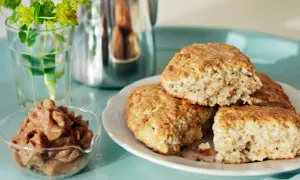 Nybakade kardemumma scones på en vit tallrik, med en skål fylld med kardemummafyllning och en vas med gröna blommor i bakgrunden.