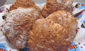 Nybakade scones med yoghurt, pudrade med mjöl, ligger i en korg med ett färgglatt mönster.