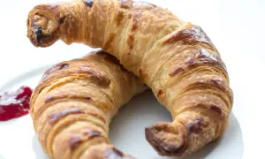 Två gyllene, krispiga croissanter på en vit tallrik med en klick sylt. Perfekt för ett croissant recept.
