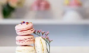 En stapel rosa och vita macarons, dekorerade med blomblad. Ett enkelt macarons recept för en vacker dessert.
