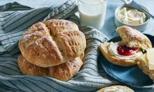 En hög med söta scones, redo att avnjutas med sylt och grädde. Ett glas mjölk står bredvid, perfekt för en mysig fika.