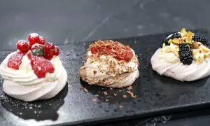 Tre små pavlovakakor med olika toppingar: jordgubbar och vinbär, choklad och hallon, samt björnbär och pistagenötter.