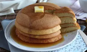 En hög med fluffiga japanska pannkakor, toppad med smör och sirap, serveras på en tallrik.