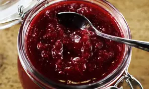 En burk med hemgjord lingonsylt, perfekt för ett enkelt lingonsylt recept. En sked vilar i den rika, röda sylten.