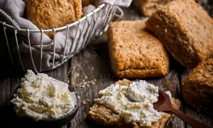 Scones med grahamsmjöl serveras med en skål krämig ost och en sked som sprider den på en scone.