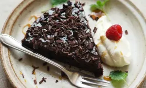 En bit kladdkaka toppad med chokladspån, serverad med vispad grädde, hallon och mynta. Perfekt för den som vill ha glutenfria kladdkakemuffins.