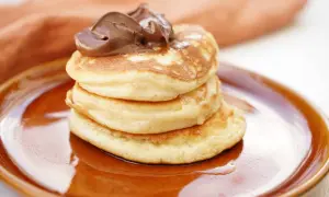 En hög med fluffiga american pancakes toppas med chokladkräm på en brun tallrik.