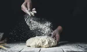 Händer strör mjöl över deg. Jämförelse mellan dinkelmjöl vs vetemjöl i bakning.