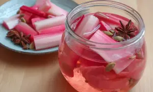 Rabarbersaft recept: färska rabarberbitar i en glasburk med kryddor som stjärnanis och kardemumma. En tallrik med rabarber och kryddor står bredvid.