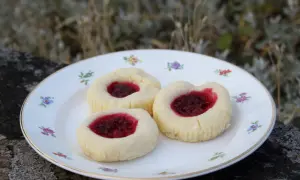 Tre glutenfria hallongrottor med sylt på en blommig tallrik.
