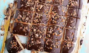 Biskvier i långpanna med chokladglasyr och krossad toffee. En gyllene kniv ligger bredvid.