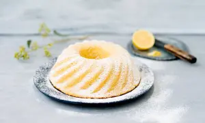 En vackert pudrad sockerkaka citron på ett fat, med en citronskiva och kniv i bakgrunden.