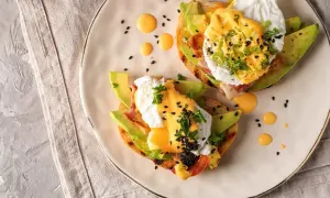 Två läckra eggs benedict på rostat bröd med avokado, bacon och hollandaisesås. Garnerade med persilja och svarta sesamfrön.