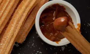 Churros coated in sugar being dipped into a bowl of dulce de leche.