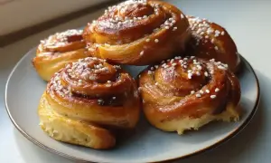 Fem gyllene kanelbullar med pärlsocker på en blågrå tallrik. Perfekt för att grädda bullar varmluft eller inte.