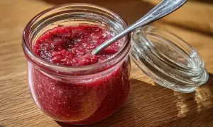 En burk med hemgjord jordgubbssylt, perfekt för ditt nästa jordgubbssylt recept. En sked vilar i sylten.