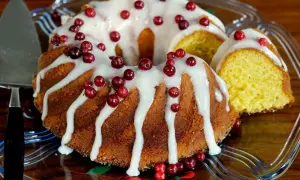 En gammaldags sockerkaka med glasyr och lingon. En bit är uppskuren och visar den gyllene insidan.