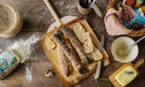 Nybakade surdegsbröd på en bakplåt, redo för ett gott surdeg recept. Ingredienser som mjöl och smör ligger utspridda.