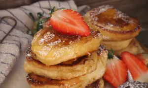 En stapel fluffiga pannkakor på filmjölk, toppade med färska jordgubbar och pudersocker.