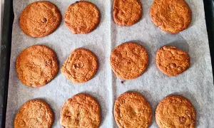 Tolv gyllene chocolate chip cookies utan farinsocker ligger på ett bakplåtspapper. De ser perfekta ut!