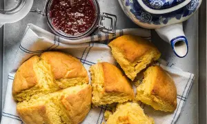 Gyllene scones majsmjöl, en burk hallonsylt och en blåvit tekanna. Perfekt för en mysig fika.