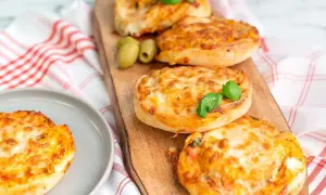Four golden-brown pizza buns topped with melted cheese and basil, served on a wooden board with olives.