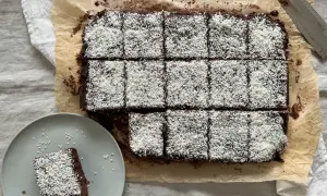 En plåt med chokladkakor, toppade med kokosflingor, redo att avnjutas som kärleksmums på påsk. En bit ligger på en tallrik.