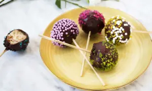 Fem chokladöverdragna cake pops med olika strössel ligger på en gul tallrik. En är uppäten.