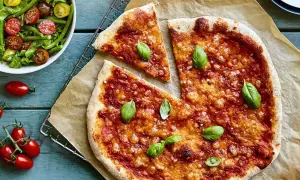 En hemmagjord pizza med nyttig pizzabotten, toppad med tomatsås och basilika. Bredvid en fräsch sallad med gröna bönor och tomater.