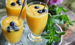 Tre glas med krämig mango smoothie, toppade med blåbär och mynta. En perfekt, uppfriskande dryck.