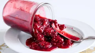 En burk med hallonsylt har vält på en tallrik, med en sked som fångar upp den läckra sylten. Perfekt för ett enkelt rosenvatten recept.