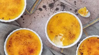 Tre vita skålar med gyllene creme brulee, en sked med en bit av desserten.